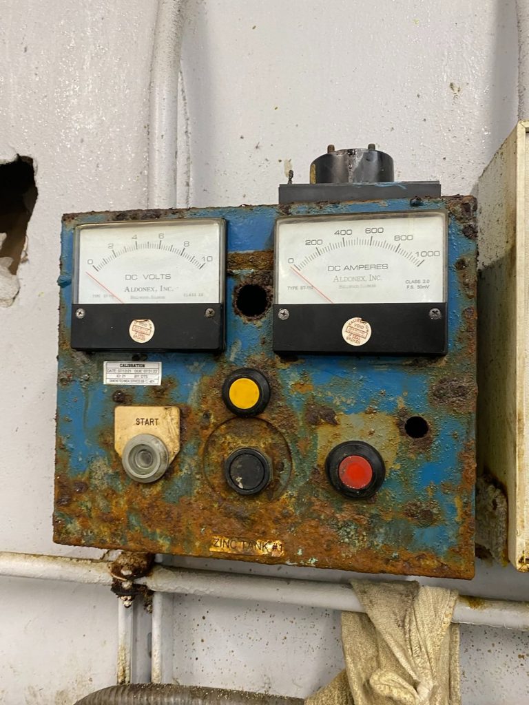 A rusty old electrical panel with two gauges.